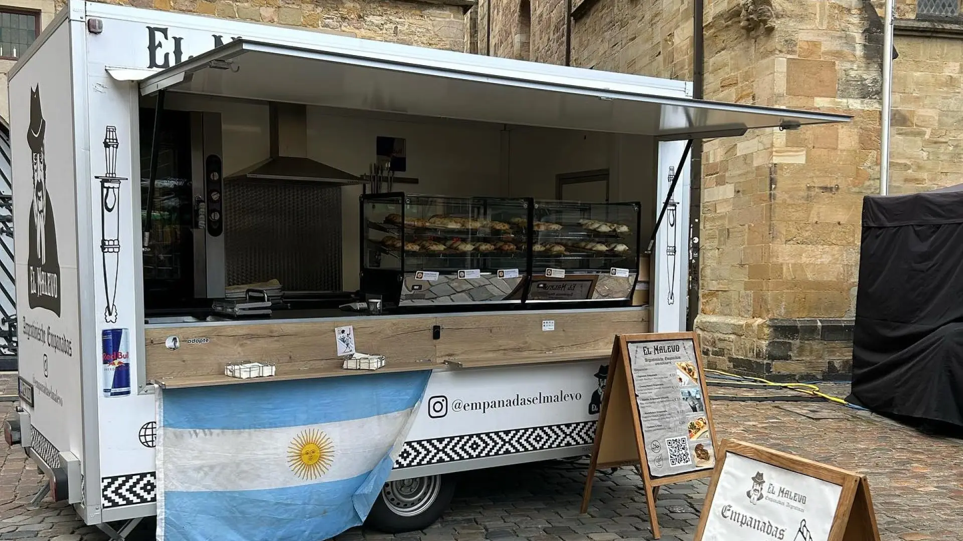 Foodtruck de El Malevo en la vía pública, con la bandera argentina y la vidriera de empanadas
